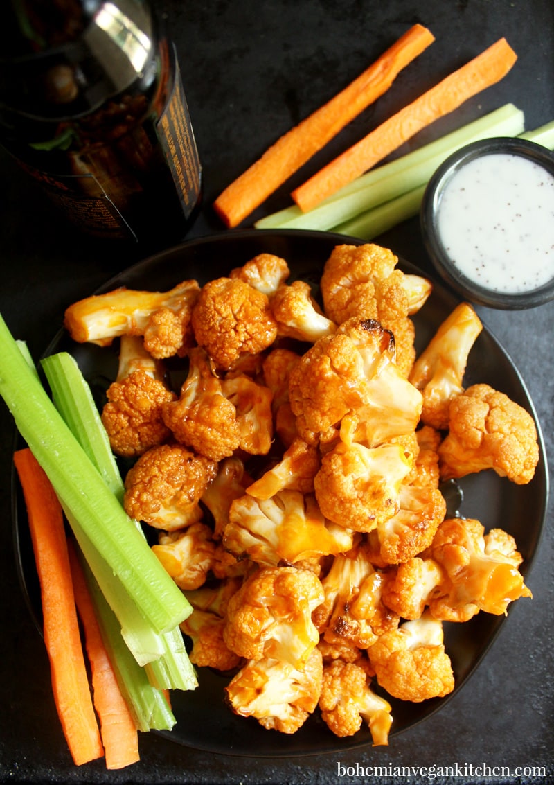 Spice up your party with these KILLER vegan buffalo cauliflower wings! Easy to pull together, you only need 10 minutes to assemble- let the oven do the rest! Serve with carrot and celery sticks, plus vegan ranch dressing to cool your taste buds. #veganbuffalocauliflower #veganbuffalocauliflowerwings #veganbuffalocauliflowerrecipes #veganbuffalocauliflowerglutenfree #bohemianvegankitchen