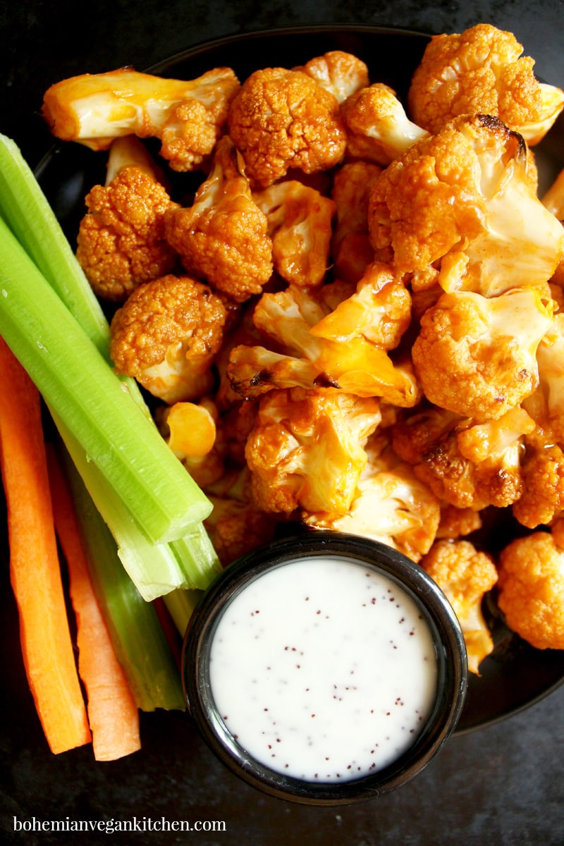 Spice up your party with these KILLER vegan buffalo cauliflower wings! Easy to pull together, you only need 10 minutes to assemble- let the oven do the rest! Serve with carrot and celery sticks, plus vegan ranch dressing to cool your taste buds. #veganbuffalocauliflower #veganbuffalocauliflowerwings #veganbuffalocauliflowerrecipes #veganbuffalocauliflowerglutenfree #bohemianvegankitchen