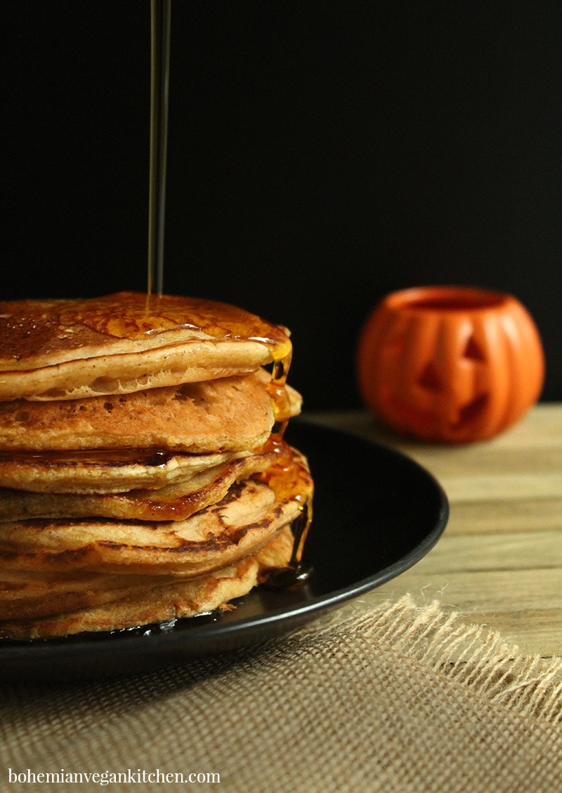 picture of vegan pumpkin pancakes on a plate with maple syrup drizzled on top.