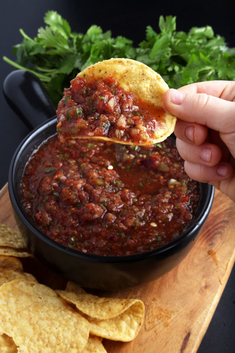 Picture of child hand lifting tortilla chip out of salsa. 