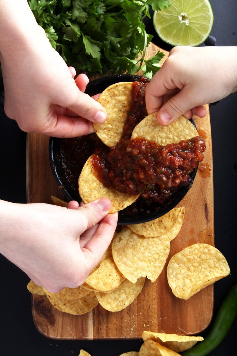 Picture of three kids hands dipping chips in salsa. 