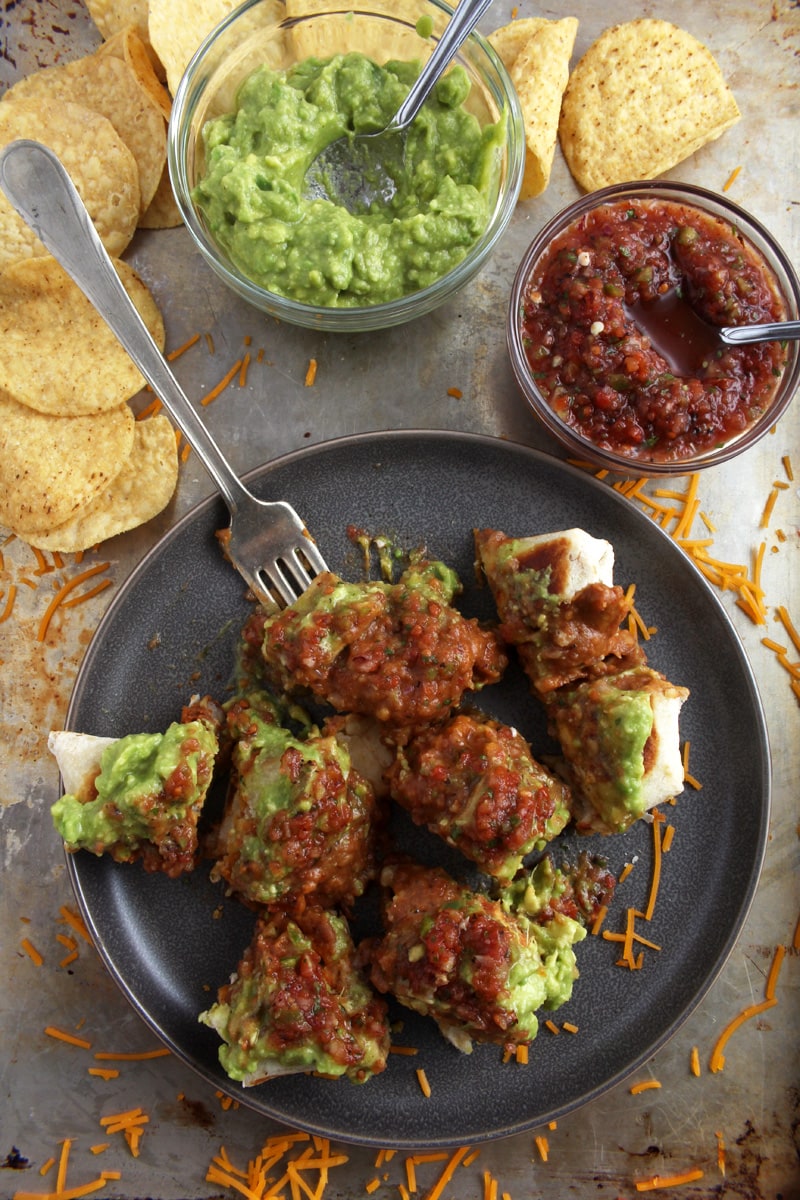 A picture of chimichangas cut up, with salsa and guacamole on top.