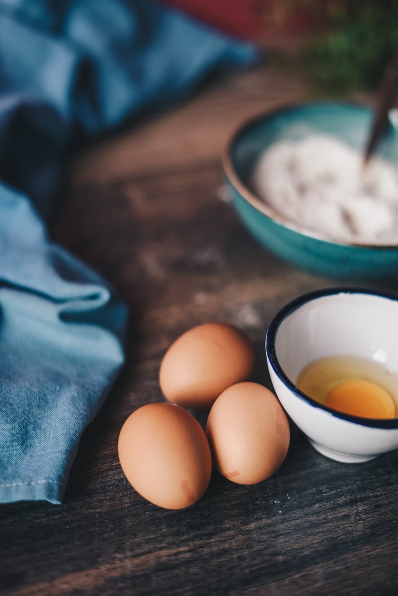 substitute eggs in baking: image of three eggs on a wooden table, a bowl with a cracked egg, and a napkin. 